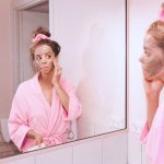 girl using creamy face scrub in the bathroom mirror